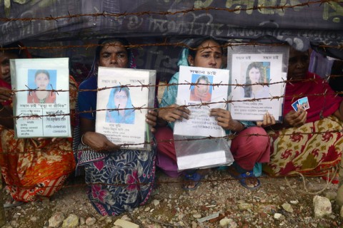Mourners hold up portraits of their missing relatives at the disaster scene during the one hundredth-day anniversary of the Rana Plaza garment building collapse in Savar, on the outskirts of Dhaka, on August 2, 2013. Credit- Munir uz Zaman/AFP via Getty Images